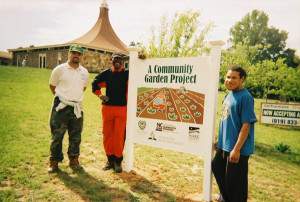 Three people standing by community garden project sign