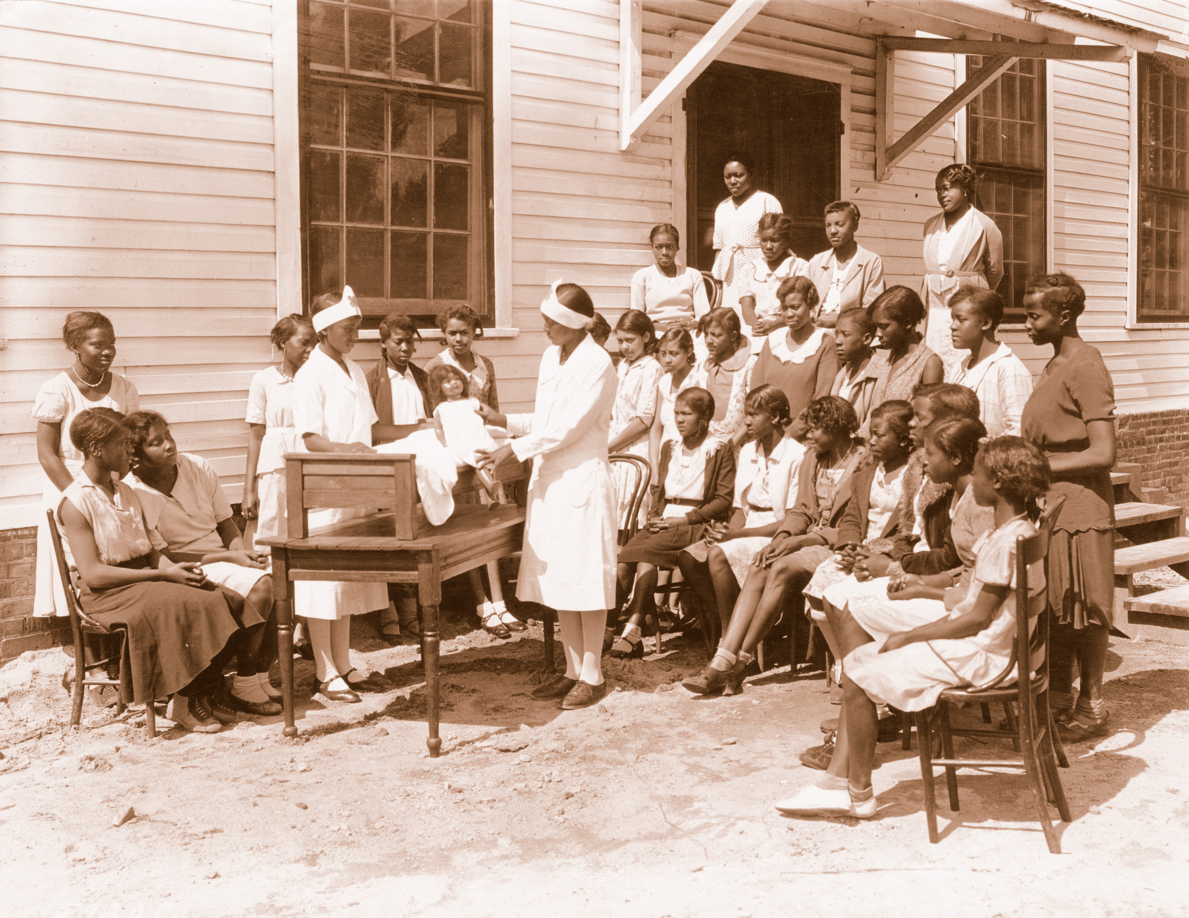 An Extension home demonstration agent discusses child care skills with a group of girls around 1930.