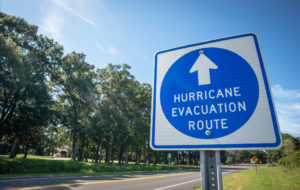 A sign next to a tree-lined road directs hurricane evacuees to safety.