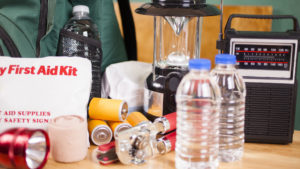 Emergency preparedness supplies. A large pile of supplies to be used in case of a natural disaster (hurricane, flood, earthquake, etc.) including: flashlight, backpack, batteries, water bottles, first aid kit, lantern, radio, can opener, mask. No people.