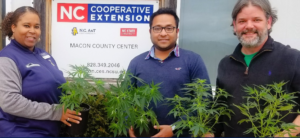Three individuals holding plants in front of an NC Cooperative Extension logo banner