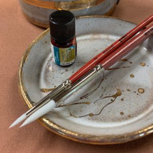 Plate with paintbrushes and vile of paint sitting on top