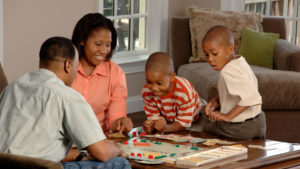 A mom and dad with their two young boys are playing a board game on the table in the living room