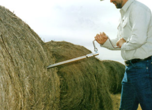 man taking core sample from round bale of hay