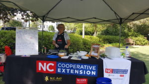 FCS Agent stands beneath a tent while providing a local food preparation demonstration