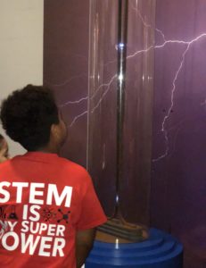 While in shirt reading STEM is my superpower gazes at an electricity experiment