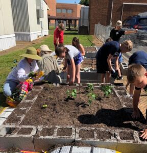 7 children and 2 adults working around 2 raised beds.