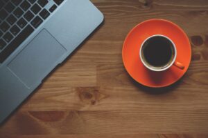 Cup of Coffee on a round orange plate and the keyboard of a laptop computer