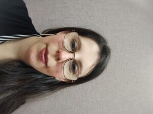 woman with brown hair and wearing glasses with a half smile