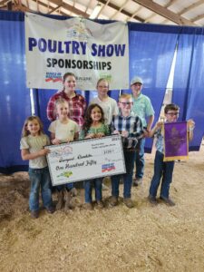 children pose with giant check award by poultry show banner