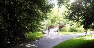 Biker comes over a bridge on a greenway that is joining with another part of the greenway.