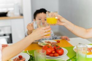 young child holding up glass to two adult hands also holding up glasses at table