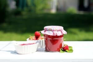 strawberry jam surrounded by fresh strawberries in white bowl and on table