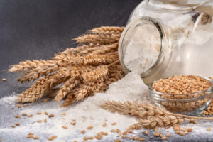 A glass jar with flour and grain sprinkled on a black background