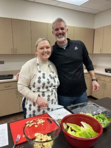 two people standing in front of a cutting board with vegetables