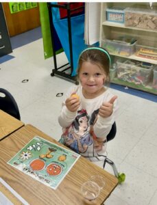 a little girl giving a thumbs up sign with a pumpkin life cycle mat on her desk