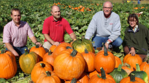 NC State Extension experts kneel in a mountain research plot surrounded by large orange and green pumpkins, highlighting Extension’s work studying and supporting pumpkin production in North Carolina.